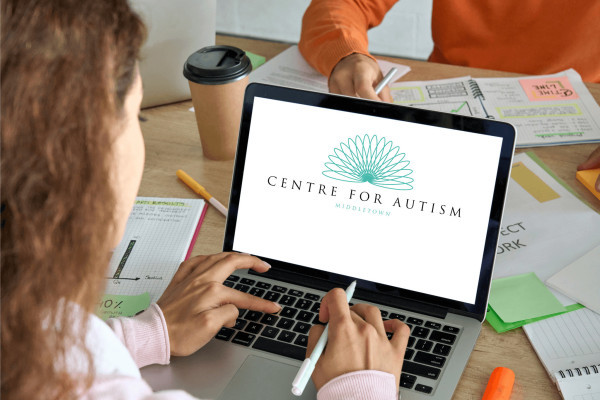 Two people collaborate at a desk with worksheets and coffee as a laptop displays the Centre for Autism logo, creating a supportive office tone.
